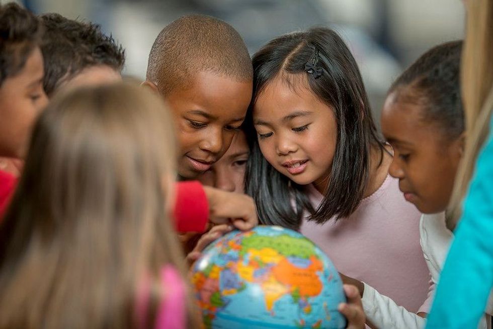 A multi-ethnic group of elementary-age students is learning the places of the world by looking at a globe.