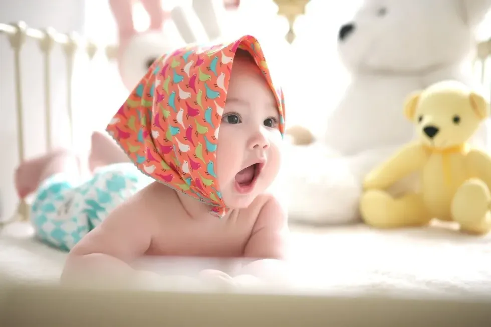 A newborn baby girl wearing a head scarf is yawning and playing with her teddy bear toys