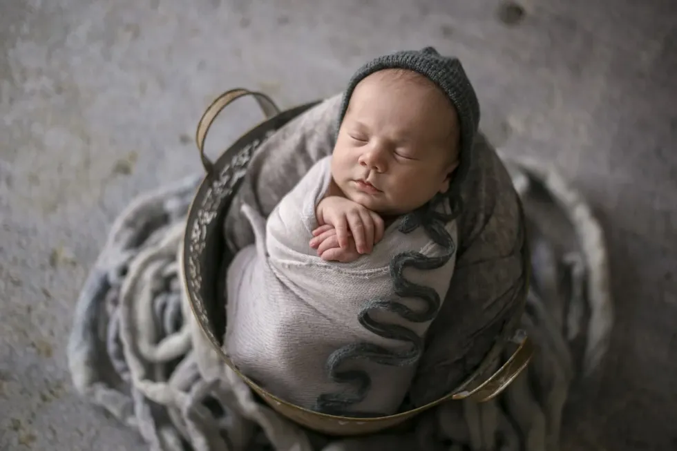 A newborn baby named after a healer sleeping in a gray basket 