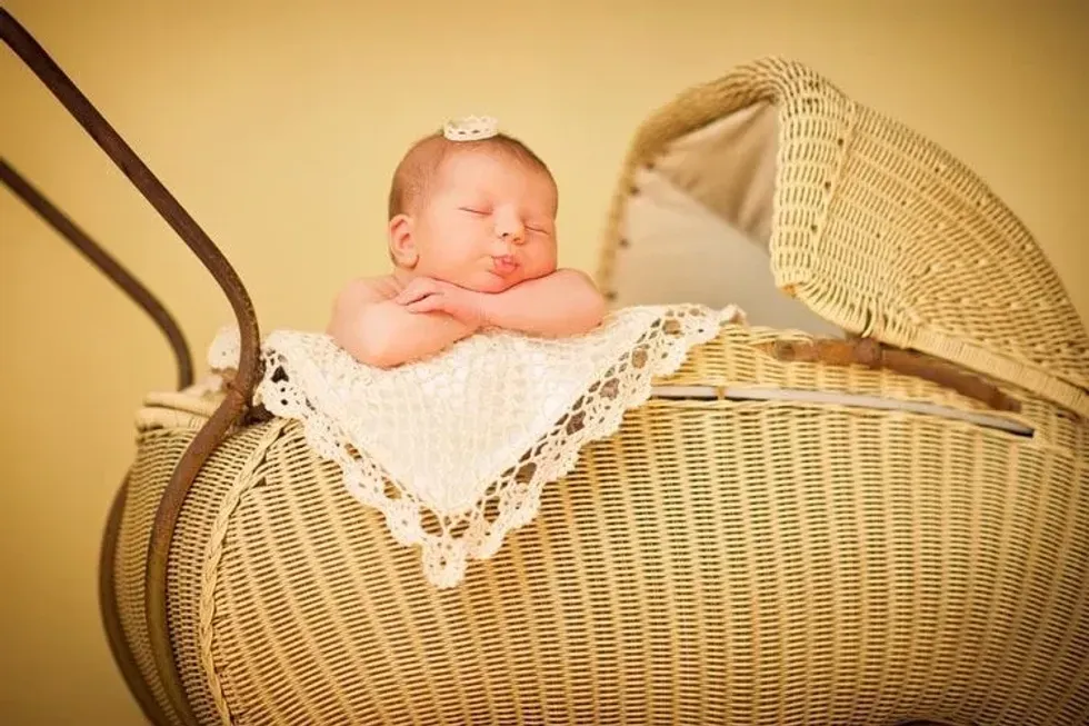 A newborn baby sleeping on a stroller wearing a tiny crown