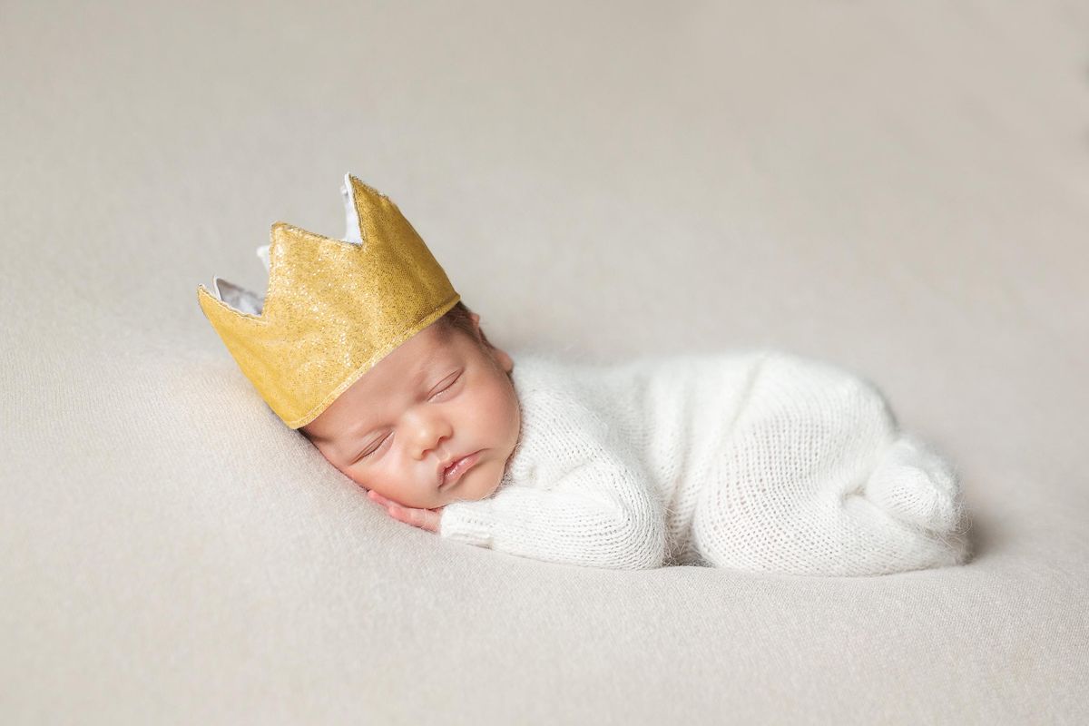 A newborn baby sleeping peacefully while wearing a golden crown, evoking images of posh boy names.