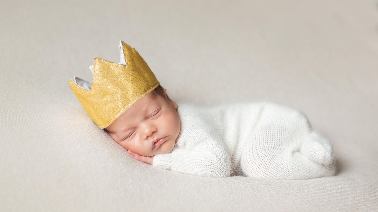 A newborn baby sleeping peacefully while wearing a golden crown, evoking images of posh boy names.