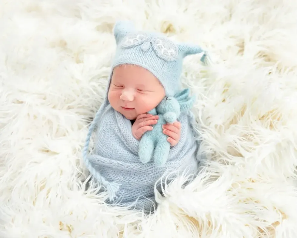 A newborn baby sleeping with blue knitted rabbit in hand.