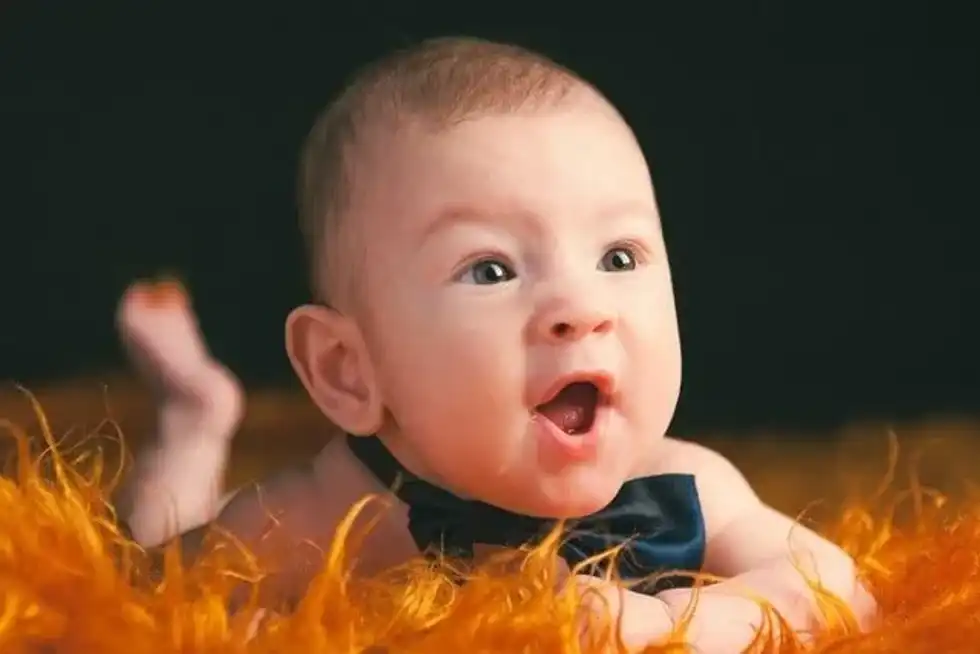 A newborn baby wearing a bow and lying on orange fur