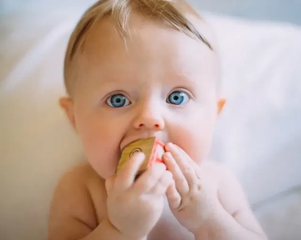 A newborn baby with blue eyes trying to chew a wooden cube toy