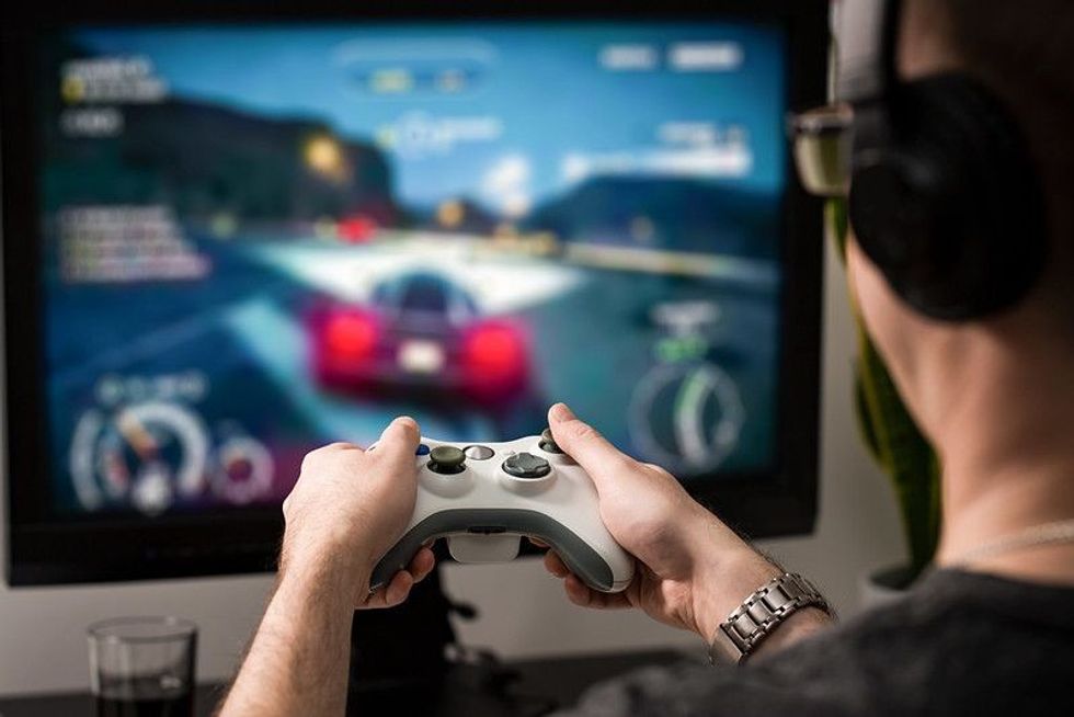 A person from behind wearing headphones playing a racing game on a TV screen with a white game controller in hands.