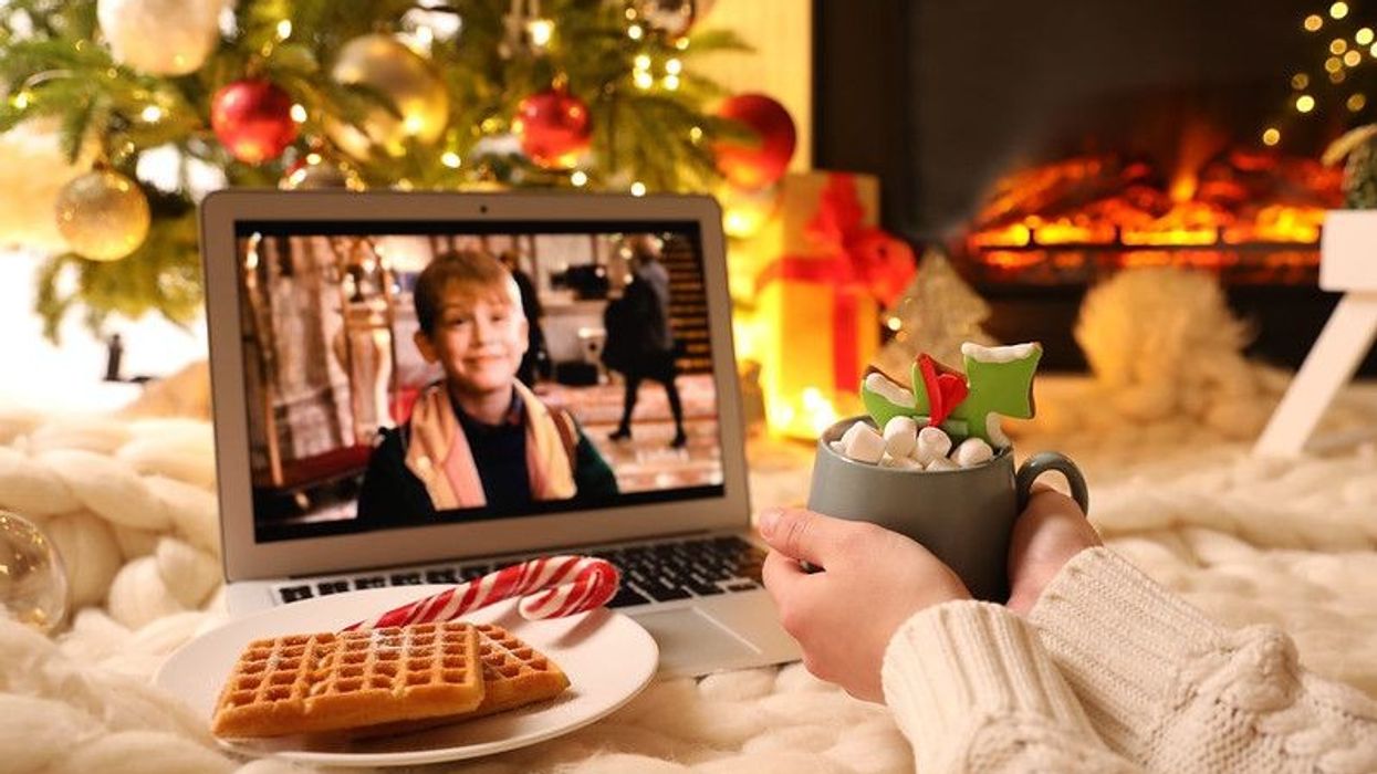 A person holding a drink watching Home Alone movie on laptop