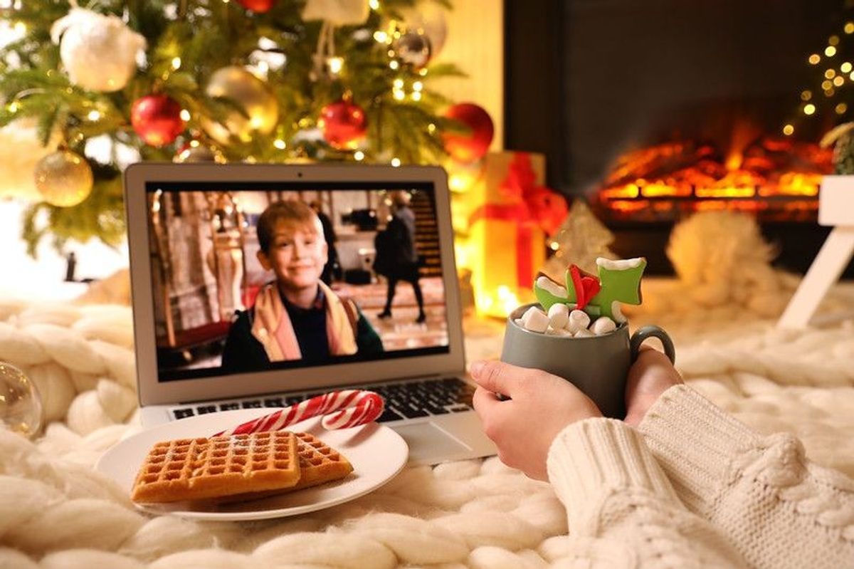 A person holding a drink watching Home Alone movie on laptop
