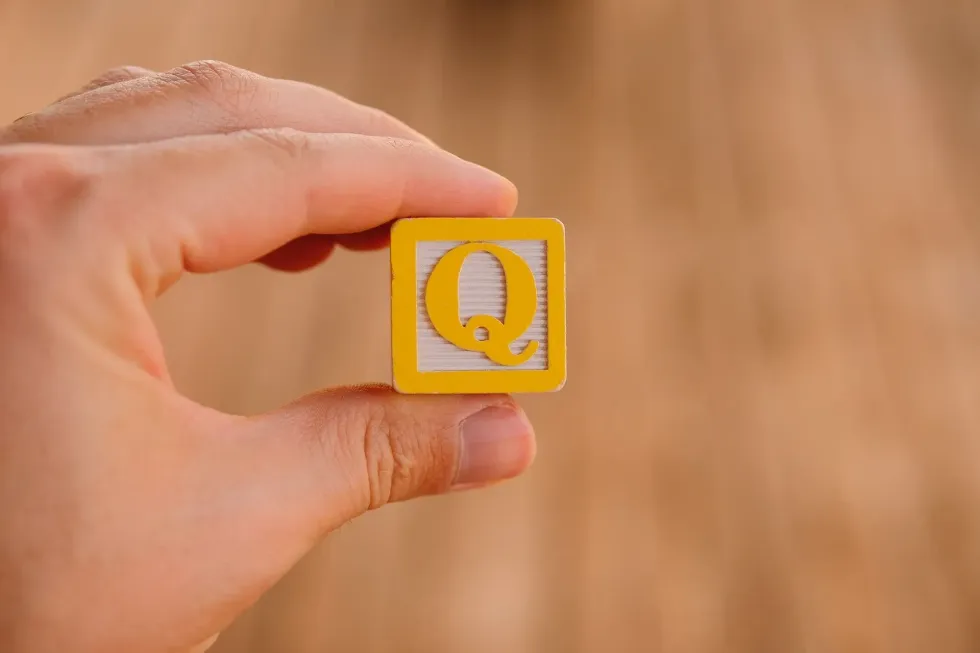 A person holding a Yellow wooden block of alphabet Q