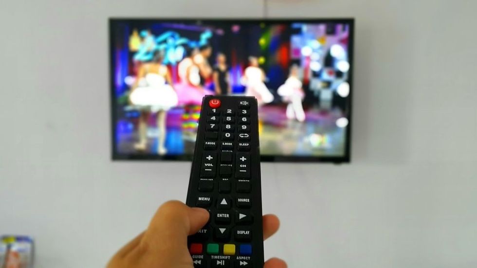 A person holding remote control with blurry background and blurry television