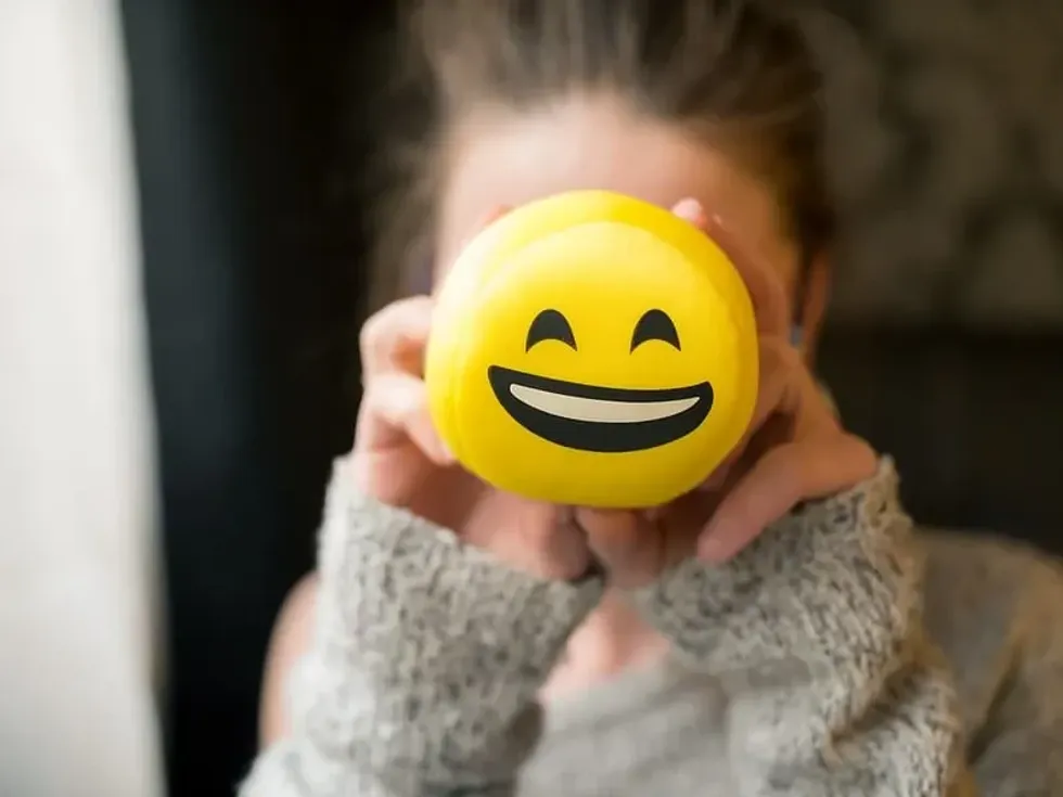A person holding up a yellow emoji craft in front of their face.