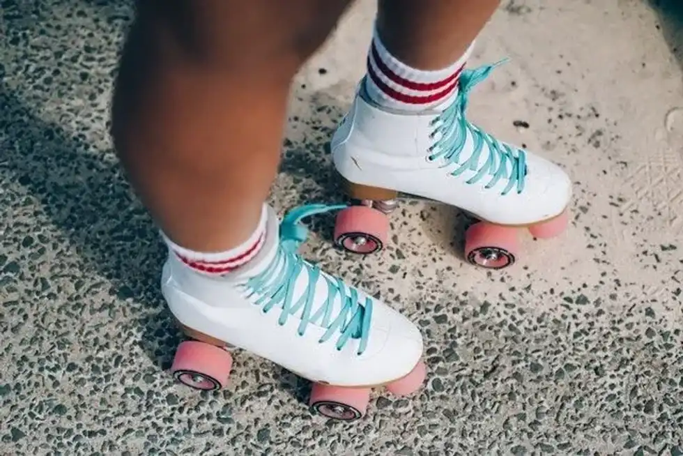 A person wearing white roller derby with pink wheels