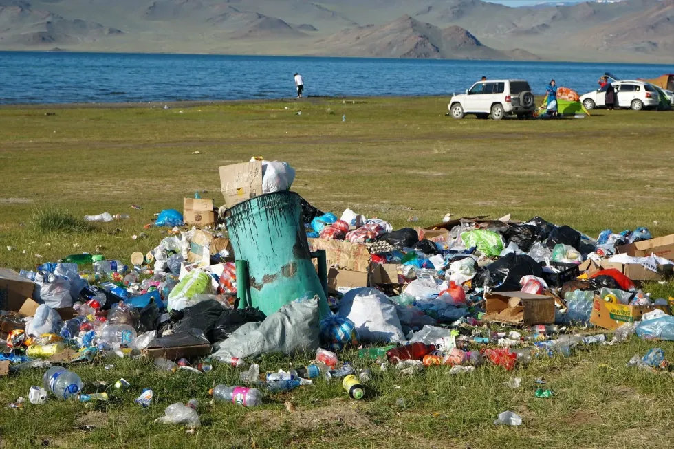  A pile of overflowing trash with a scenic lake and mountains in the background.