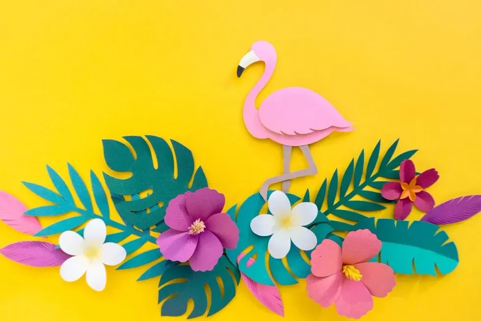 A pink origami flamingo which looks as if it's walking on some origami flowers stuck on a yellow background.