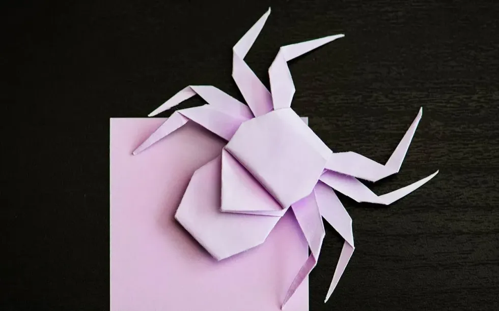 A purple origami spider next to a pile of origami paper.