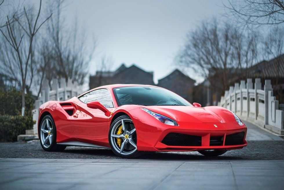 A red Ferrari 488 GTB parked in front of a stone bridge.