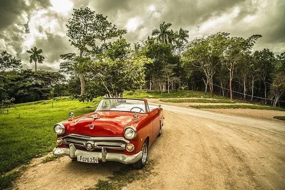 A red vintage car parked on a dirt road beside a grassy field.