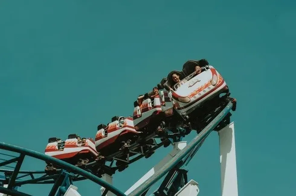  A roller coaster car descends rapidly with excited riders against a clear teal sky.