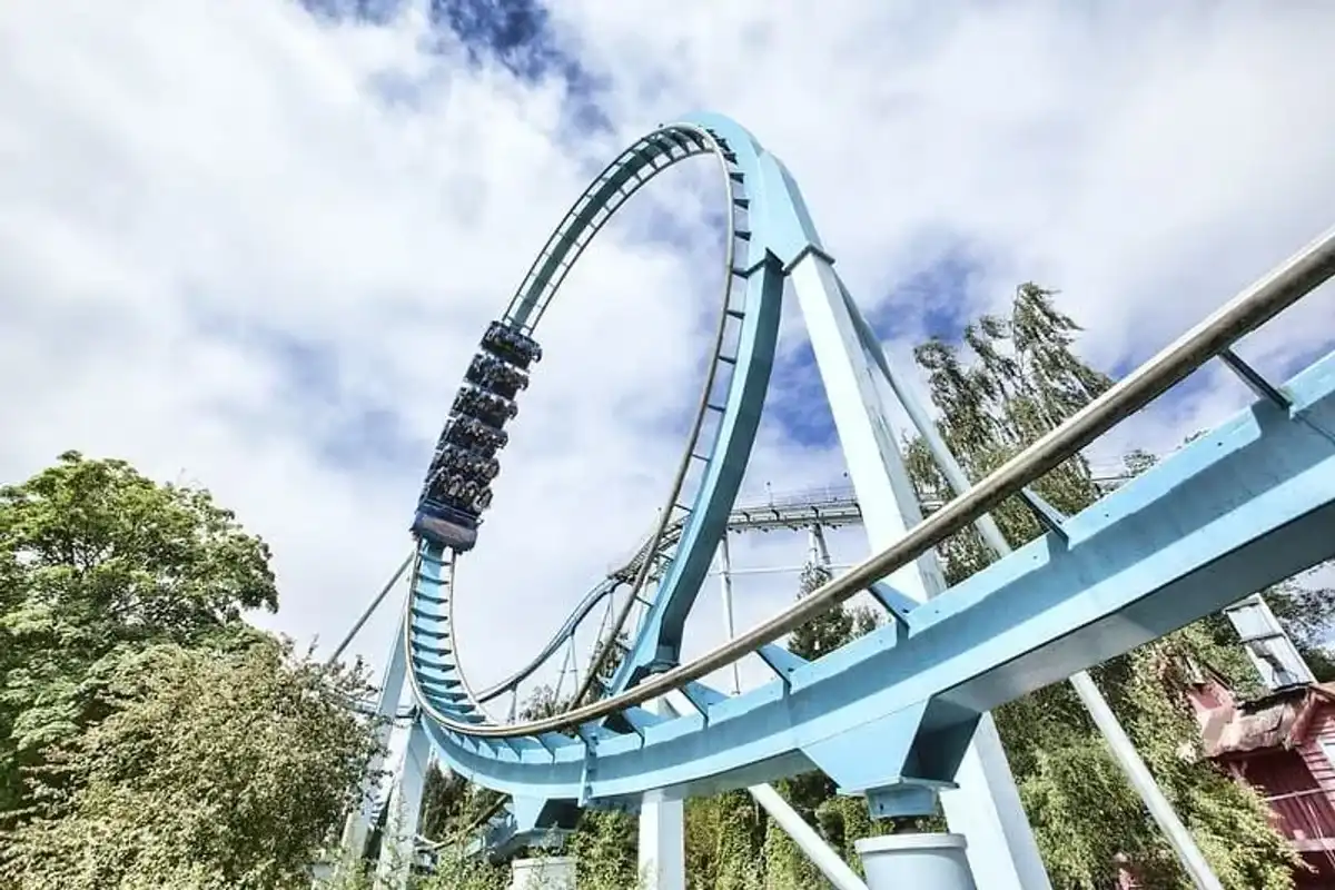 A roller coaster car filled with people is on an inverted loop amidst lush greenery and a partly cloudy sky.
