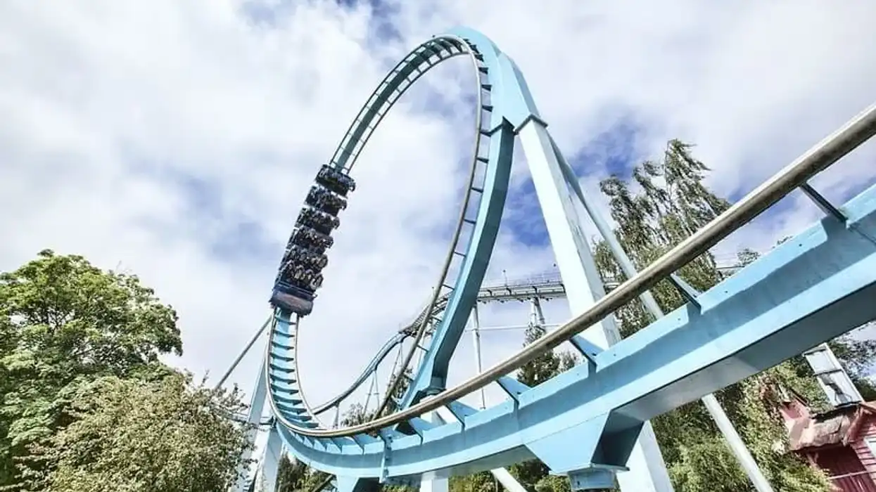A roller coaster car filled with people is on an inverted loop amidst lush greenery and a partly cloudy sky.
