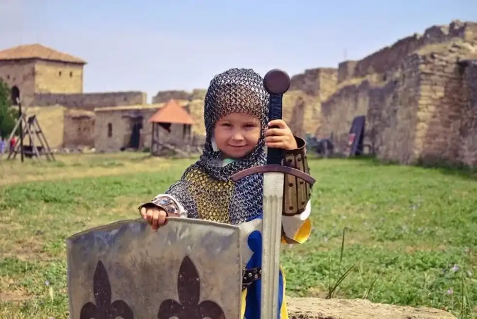 A small but very brave girl in armour and chain mail with sword and shield in a medieval castle