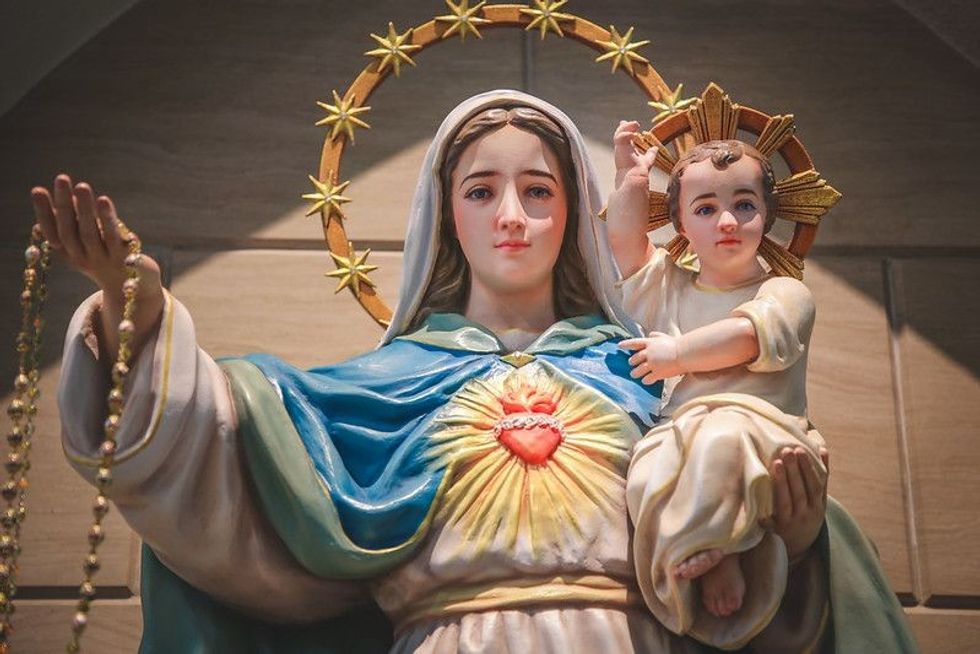 A statue of Mother Mary holding her child, Jesus, in a catholic church setting.