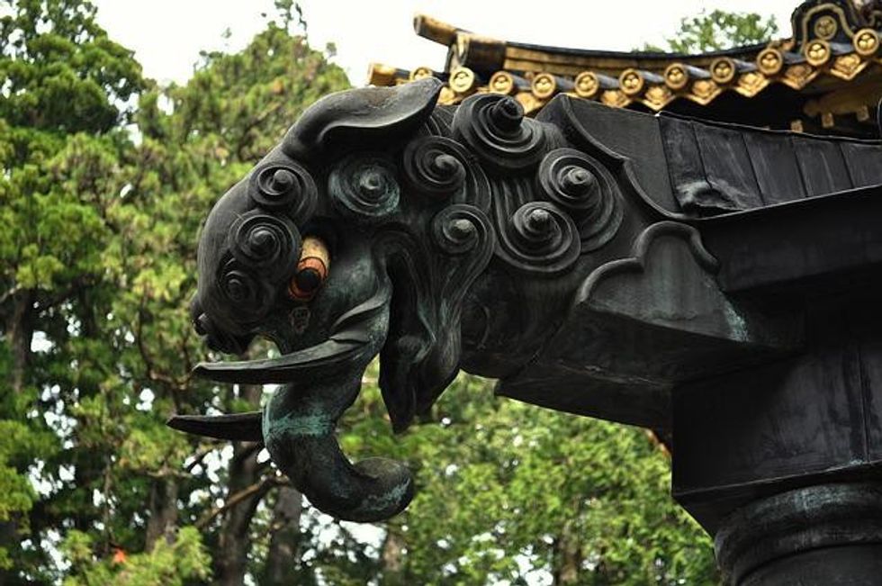 A traditional Japanese oni sculpture with swirling patterns, protruding horns, and a fierce expression, adorning a temple rooftop.