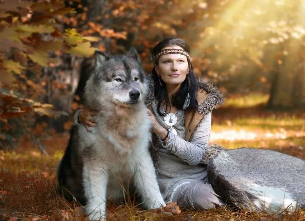 A woman is sitting beside a werewolf dog