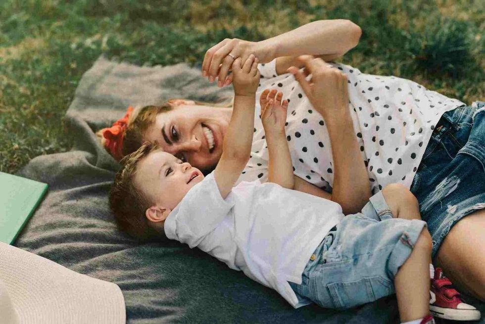 A woman laying on a blanket on a grass beside a little boy, both of them smiling.
