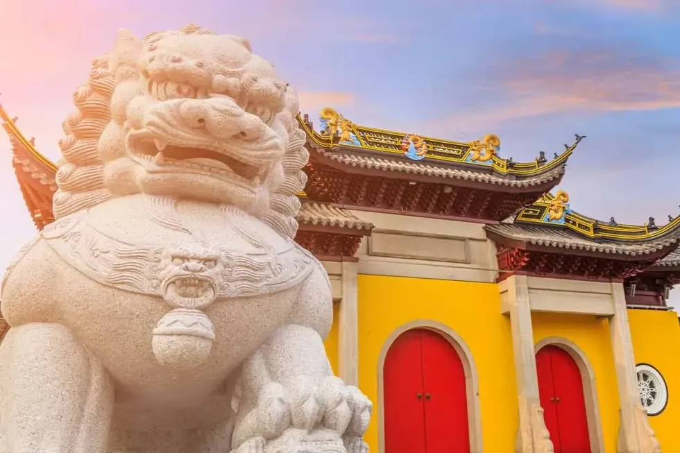 A yellow and red Chinese temple with a statue in front of it.