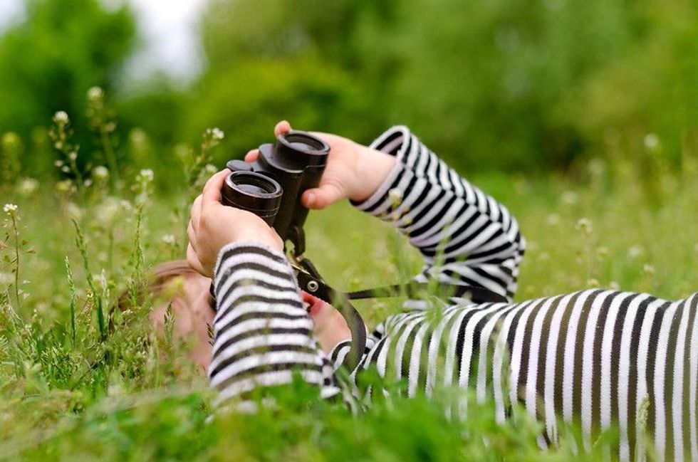 A young child engaging in outdoor adventures, using a pair of binoculars to look up into the sky