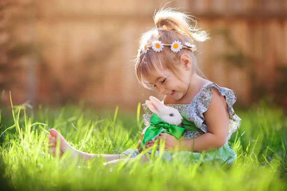 A young girl with flowers in her hair sits in sun with her pet rabbit