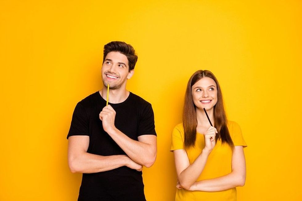 A young man and a lady holding pencils and smiling in a thinking post.