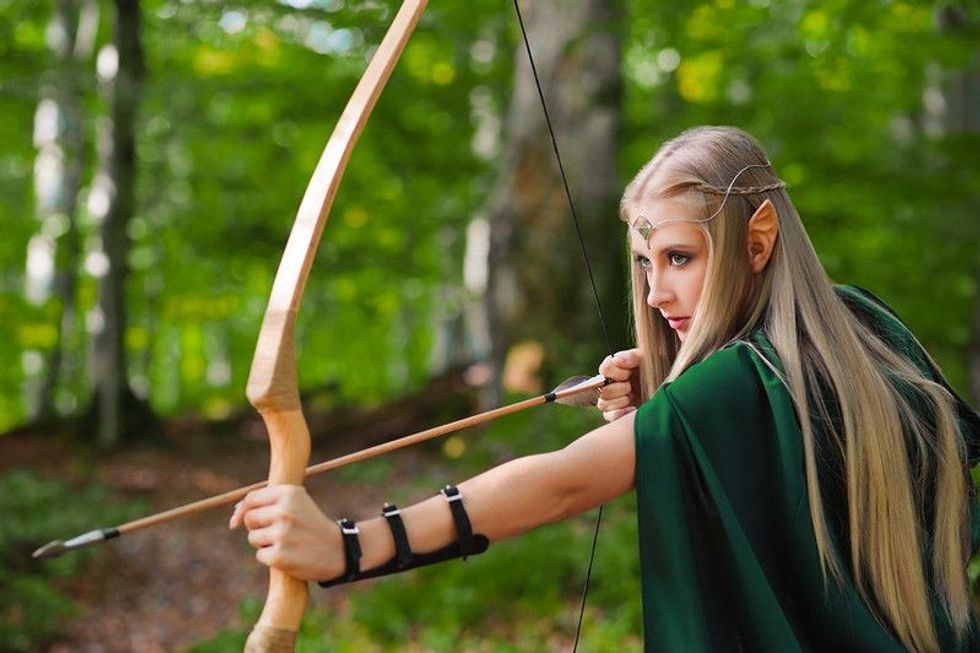 A young woman dressed as an elf with her arrow in the jungle.