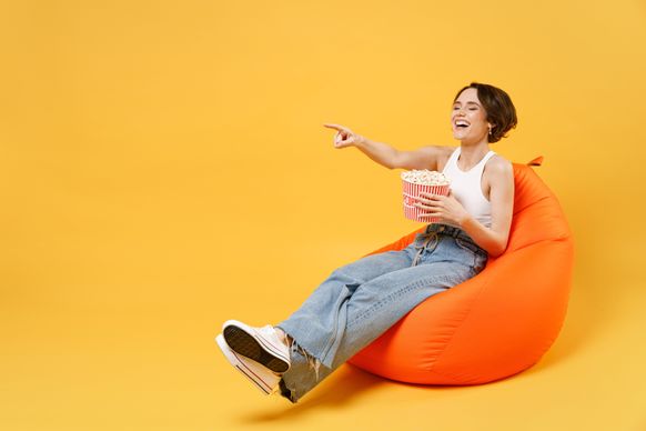 A young woman sitting on a chair in a plain yellow background and laughing.