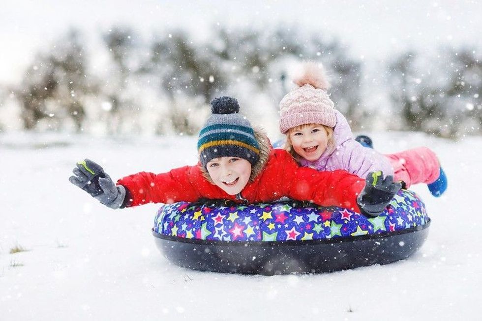 Active toddler girl and school boy sliding together down the hill on snow tube.