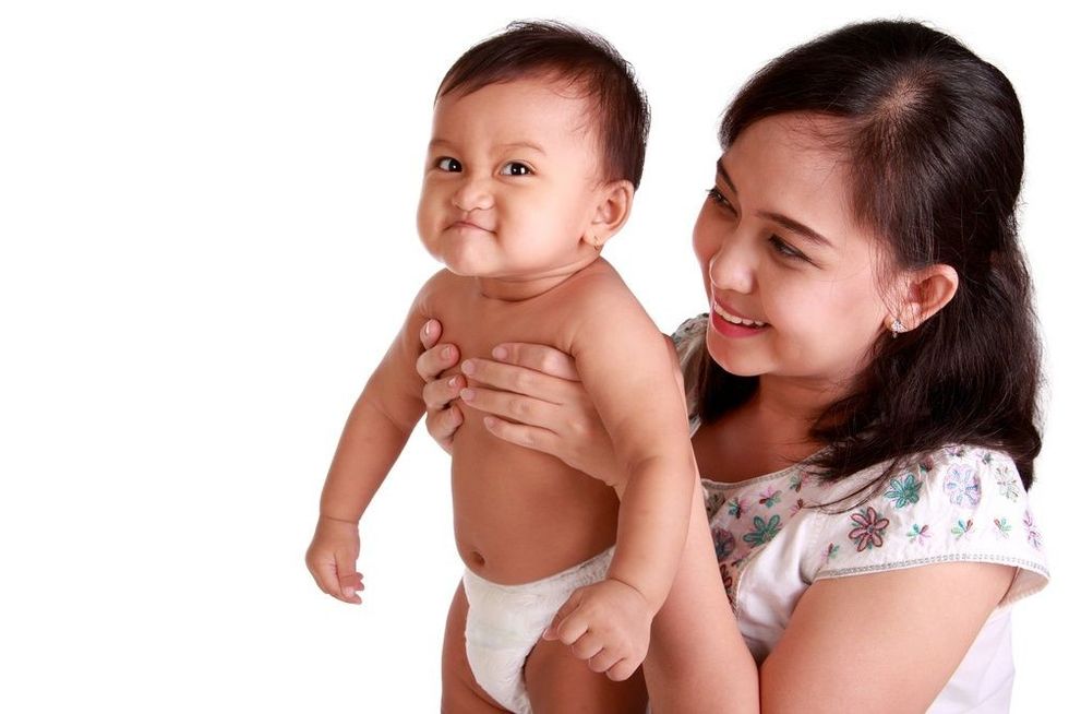 Adorable baby girl making a funny face expression while lifted by her mom.
