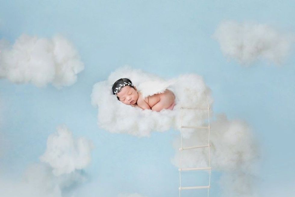 Adorable baby sleeping on clouds in blue sky like little angel