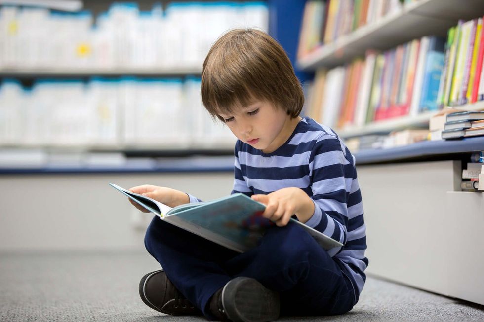 Adorable little child reading book in library.