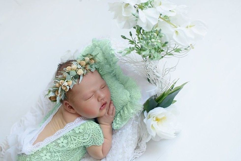 Adorable little newborn baby girl sleeping next to flowers.