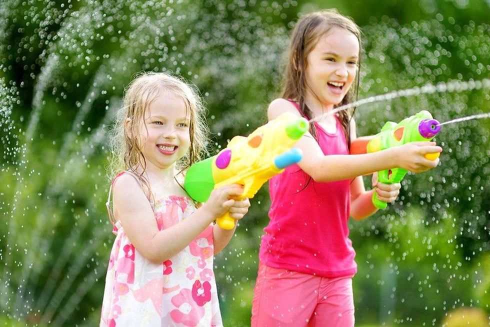 Adorable young girls playing with water guns on hot summer day.