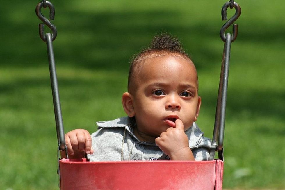American Baby in Swing with Finger in his mouth.