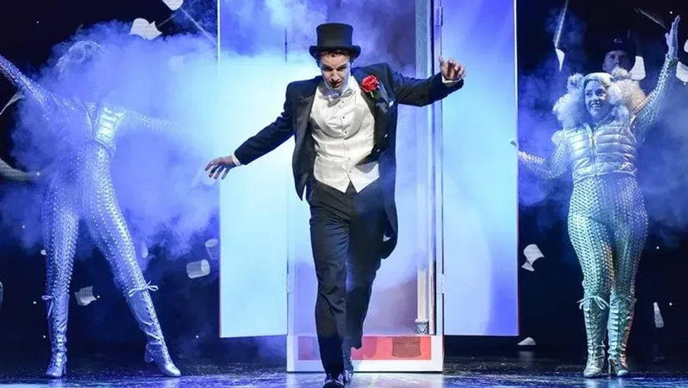 An actor in a magician's suit coming out of a door on stage at Magic Goes Wrong.