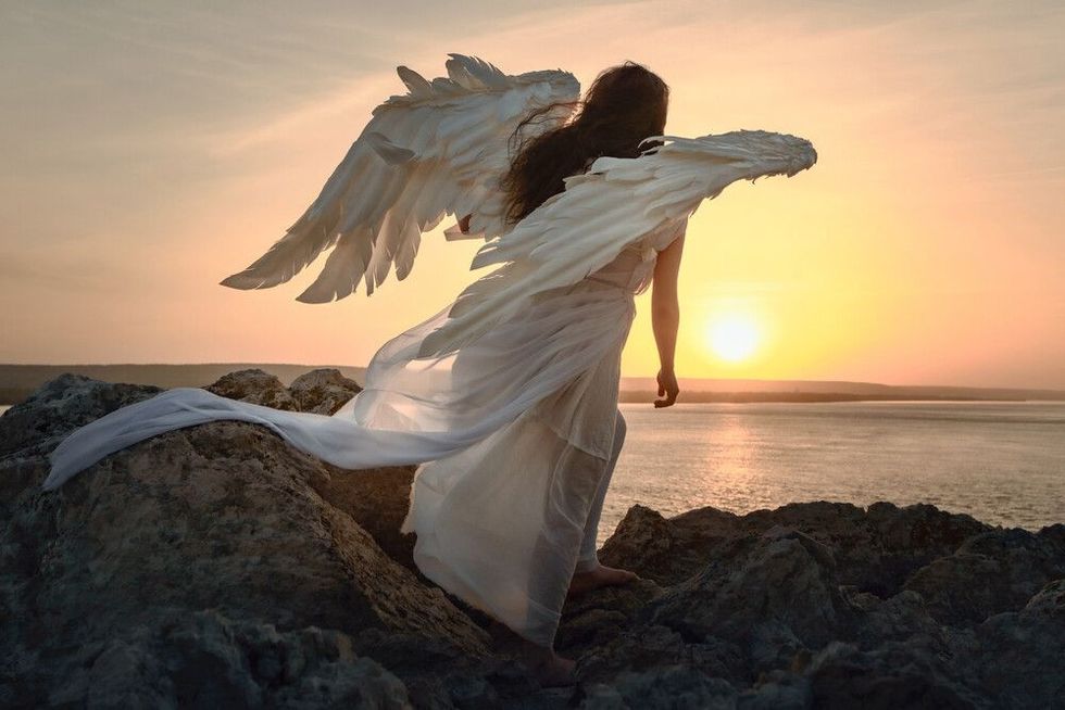 an angel girl with big white wings stands on a mountain at dawn
