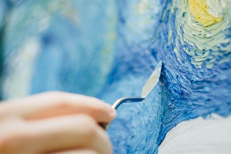 An Artist holding a mastekhin smeared in oil paint and painting Van Gogh's starry night replica.