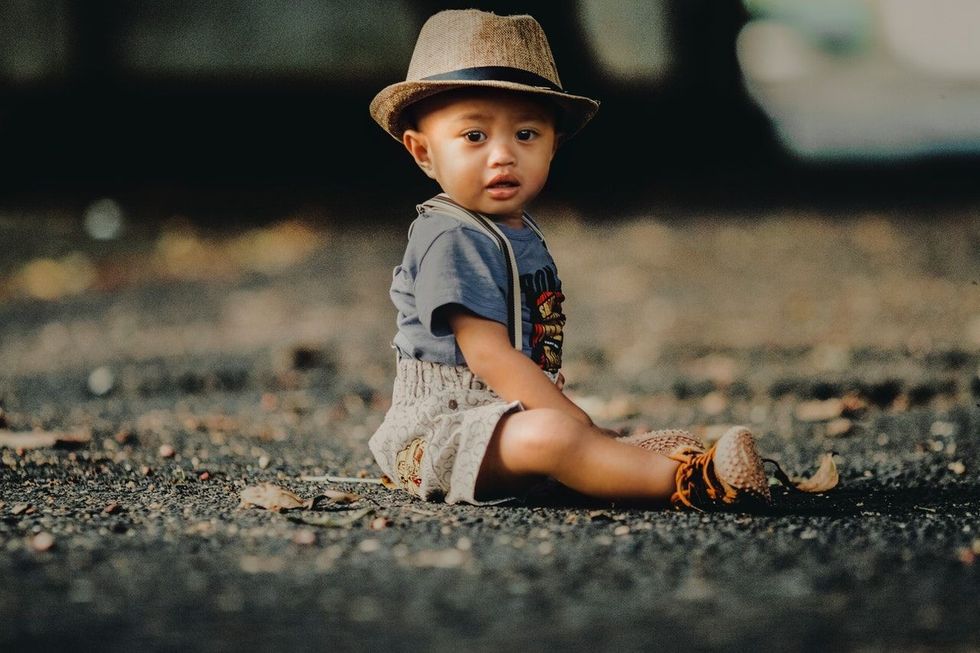 An image of a baby wearing a hat and sitting outdoors.