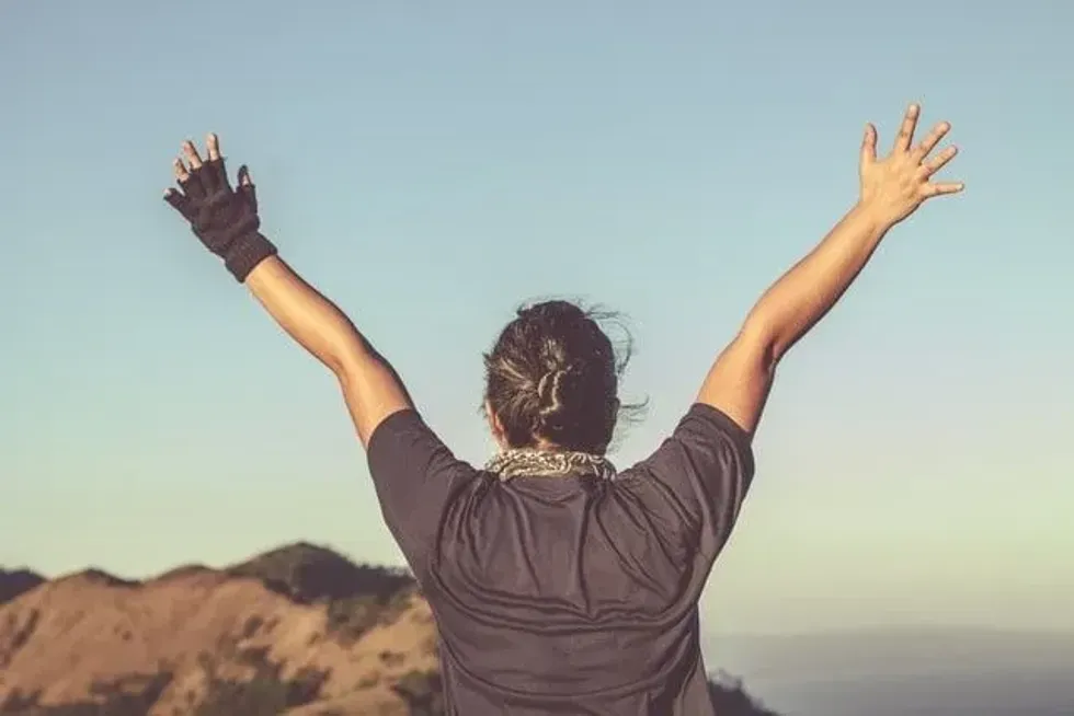 An image of a lady raising her hands on the top of a mountain.