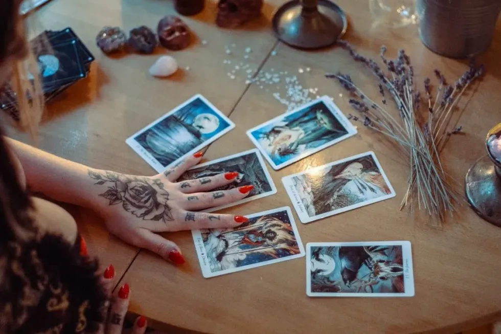 An image showing a hand with flower tattoos and red nail polish trying a psychic reading on a 6 set of images displayed in front of her