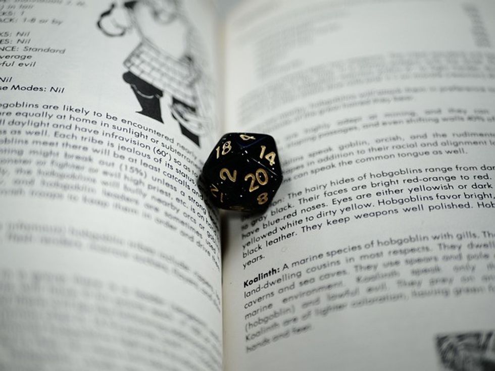 An open book with a mythical-themed dice in between its pages.