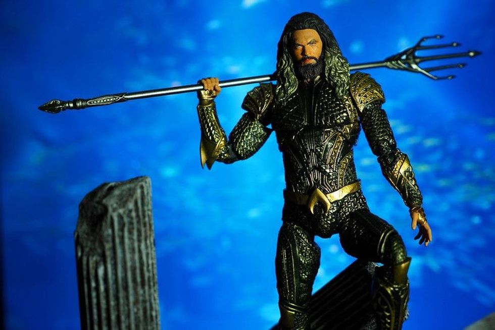 Aquaman dressed in his superhero armor holding a trident across his shoulders.